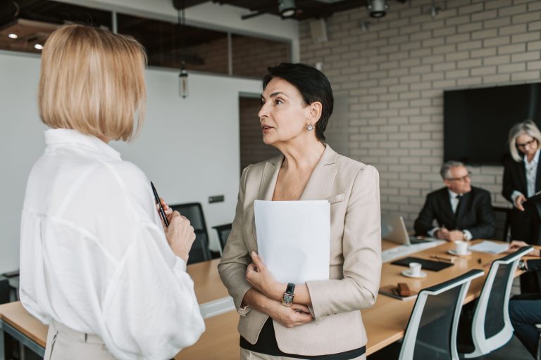 Two women talking beside a meeting table in an office.