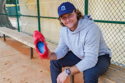 Brendan Donovan Moves With Blu Brendan Donovan, a professional baseball Second Baseman, holds a red baseball cleat with a Blumaka Konnect insole inside. He is sitting in a baseball dugout and wearing a gray sweatshirt and a Navy blue baseball cap with a Blumaka logo.