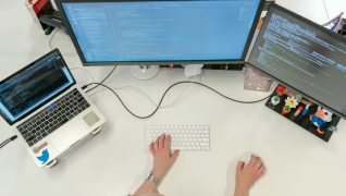 A person working at two monitors and a laptop displaying code.
